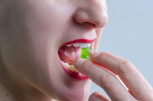 Close up on woman eating green gummy bear Close up of woman eating a green gummy bear seen from side with white background eating gummies stock pictures, royalty-free photos & images