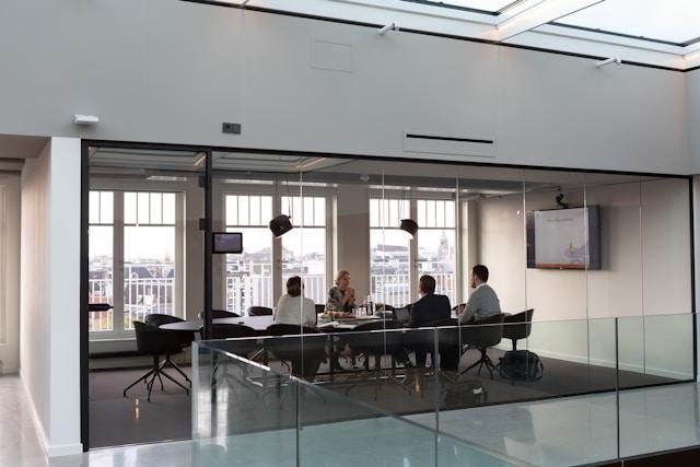 A group of people sitting around the table in an office with glass doors and windows.